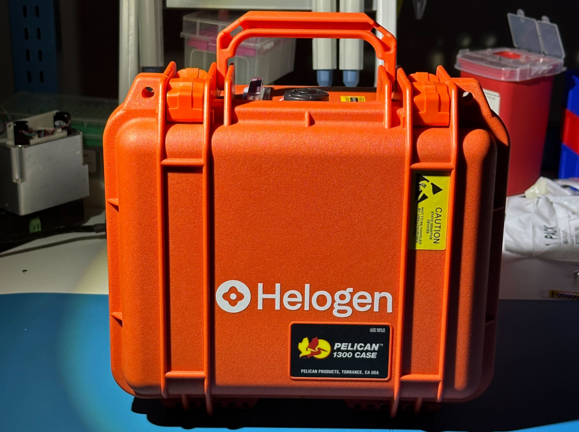 White Helogen symbol and wordmark on an orange Pelican equipment case in a lab